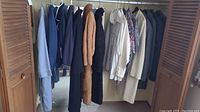 Various blazers, jackets, fur coat, and shirts hanging on a closet rod