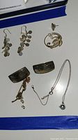 Top view of assorted jewelry pieces on white card including dangle earrings, brooch, necklace, and curved cuff pieces.