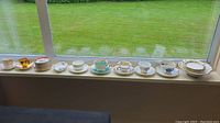 Miniature china teacups, saucers, and plates arranged on a window ledge showing the full set