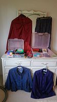 Red Ralph Lauren cape hanging next to dark blue skirt. On dresser below, two jackets, multiple accessories and shoe boxes visible.