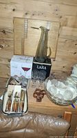 Photo showing tinted glass pitcher, punch bowl with glasses, wine glasses in original boxes, vintage flatware in trays, and wooden napkin rings.