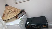 Photo showing Telefunx reel to reel tape recorder on top of a white mechanical device, Asian-style parasol partially open beside it, and black suitcase on the floor.