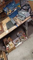 Overview of the lot showing a wooden table with multiple items including a toolbox, rolls, boxes with small hardware items and hand tools.