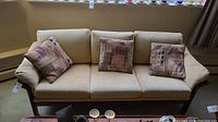 Front view of vintage wood and upholstered sofa with three square cushions and matching patterned throw pillows.