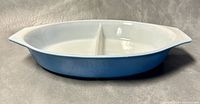 Side angled view of 12 inch light blue and white oval Pyrex split casserole dish showing the two compartments and handle.