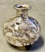 Close-up photo of small round glass bottle with sterling silver floral and scroll overlay.