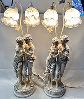 Front view of the pair of figural table lamps lit, showing the embracing couple and frosted glass shades