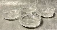 Four clear textured icicle pattern glass bowls shown together on neutral surface