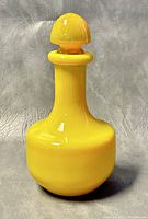 Front view of yellow glass decanter with stopper on grey background