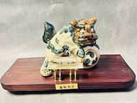 Front view of the ceramic Foo Dog sculpture on wooden base with metal plaque