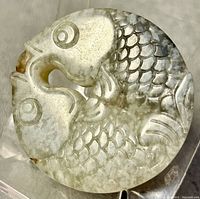 Close-up front view showing detailed carving of two goldfish in a circle shape with natural jade coloration.