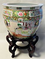 Front and side view of the large hand painted jardiniere on its wooden stand, showing detailed painted scene and floral decoration.