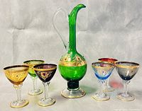 Seven-piece vintage Italian colored glass liquor set arranged with decanter in the middle surrounded by six goblets in various colors on a neutral backdrop
