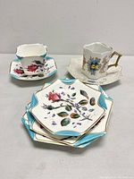 Overall view of 7-piece English Victorian porcelain set with 2 distinct cups, 2 saucers, 3 lozenge-shaped side plates showing floral designs and gold trim.