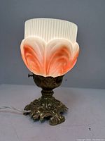 Side view of antique gilt metal table lamp with two-tone art glass shade featuring white and orange petal pattern.
