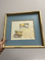 Framed watercolour painting with blue mat and bamboo-effect frame held in hand for scale.