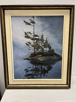 Front view of the framed oil painting showing an island scene with pine trees and their reflection in water, signed by Roxana Dyck.