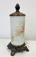 Front angled view of the lamp showing the frosted art glass shade with painted floral design and ornate metal base with finial on top.