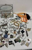 Full view of assortment showing necklaces, bracelets, brooches, earrings arranged on table with glass jewelry box