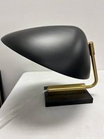 Side angle view of the stylized black metal table lamp showing the aerodynamic shade and brass pivot arm on black base.
