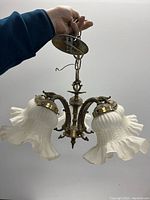 Vintage brass ceiling lamp held by hand, showing three frosted glass shades with ruffled edges and brass fixtures.