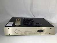 Front view of preamplifier with gold faceplate, buttons, remote on top and power cord