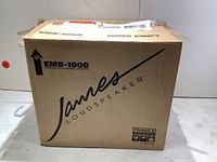 Original cardboard shipping box with James Loudspeaker branding, EMB-1000 model label and fragile handling icons.