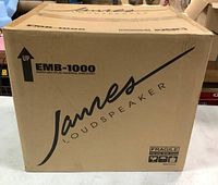 Front view of sealed James Loudspeaker EMB-1000 subwoofer box showing branding, model and fragile handling icons