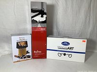 Three boxed photography gear items: Savage Macro Art LED light, Manfrotto Befree tripod, Wolverine F2D Titan film to digital converter, arranged on a neutral background.