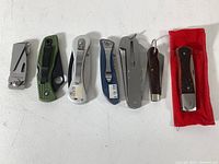 Seven folding pocket knives lined up on white background