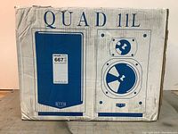 Front of sealed Quad 11L speaker box showing printed images of speaker cabinets and model name.