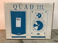 Front of white cardboard box showing QUAD 11L branding and speaker graphics in blue.