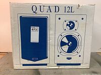 Front of cardboard box printed with “QUAD 12L” and stylized speaker illustrations
