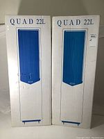 Two white Quad 22L speaker boxes side by side showing front packaging graphics.