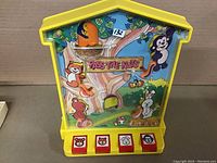 Front view of the yellow plastic "Pass-the-Nuts" push-button game with colorful animal drawings and four red buttons at the bottom.