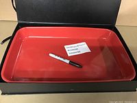 Rectangular glossy red cooking tray, new and unused, shown inside black presentation box with Sharpie marker for scale.