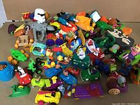 Overhead image showing a variety of colorful toy vehicles, trucks, boats, and character figurines piled together.