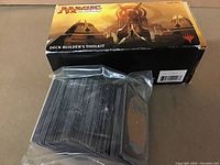 View of the Deck Builder's Toolkit box with a stack of cards in plastic wrapping leaning against it, showing Magic the Gathering card backs.