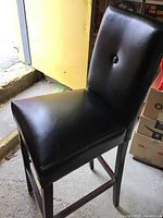 Close-up image of black bar stool showing padded leather-like seat, wooden legs, and button tuft on backrest.