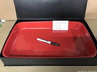 Photo showing the red rectangular cooking tray with a marker inside to indicate scale, inside a box.