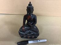 Full view of the seated statue with black and copper tones alongside Sharpie marker for scale.
