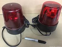 Photo showing two red rotating effect lights with black bases and power cords alongside a black marker for scale.