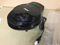 Black Parini branded waffle maker with power cord coiled beside it on beige surface.