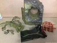 Overview photo of four main pieces: green rocky wall, green tree stump with branches, red net cage, and black rubber creature head with wear.