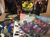 Overview of the lot showing Star Wars Customizable Card Game expansion set, Star Wars themed magazines, POGs, and stickers on a flat surface.