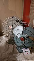 Three vintage General Electric metal table top fans with red GE logos in wire protective cages, showing some rust and signs of use.