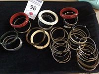 Top view of all bangle bracelets laid on black cloth showing mix of carved, lucite, metal bangles.