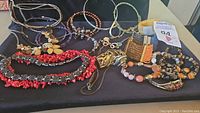Overview of various bracelets and necklaces laid on black cloth, showing diversity in styles including coral bead choker, metal cuffs, and beaded bracelets.