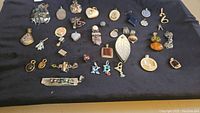 Top-down view of all pendants arranged on dark cloth showing variety and quantities in lot including pendants of different shapes and sizes, stones, and lockets.