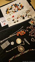 Top view of assorted broken jewelry pieces, loose beads, and stones laid out on cloth and paper towel displaying variety of colors and materials.